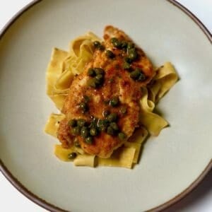 A bowl with chicken piccata served over pappardelle pasta.
