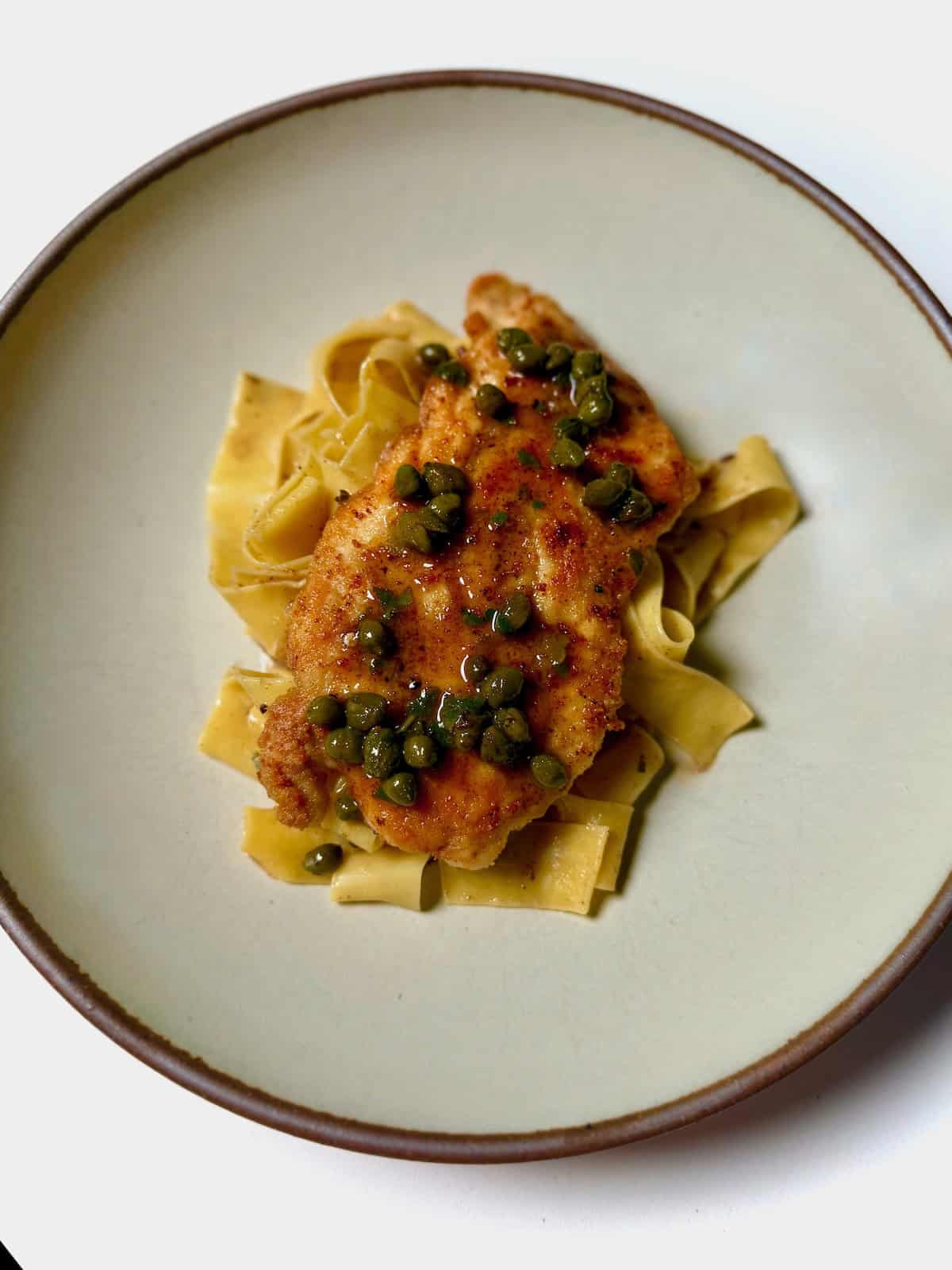 A bowl with chicken piccata served over pappardelle pasta.