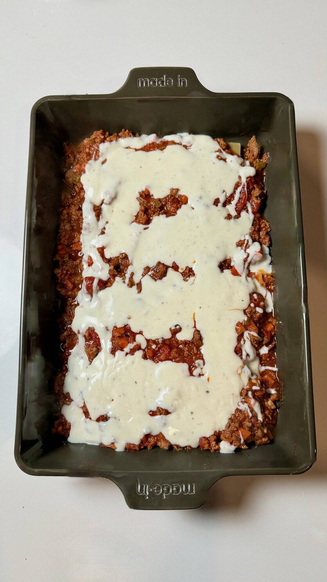 Béchamel layered on meat sauce in pan.
