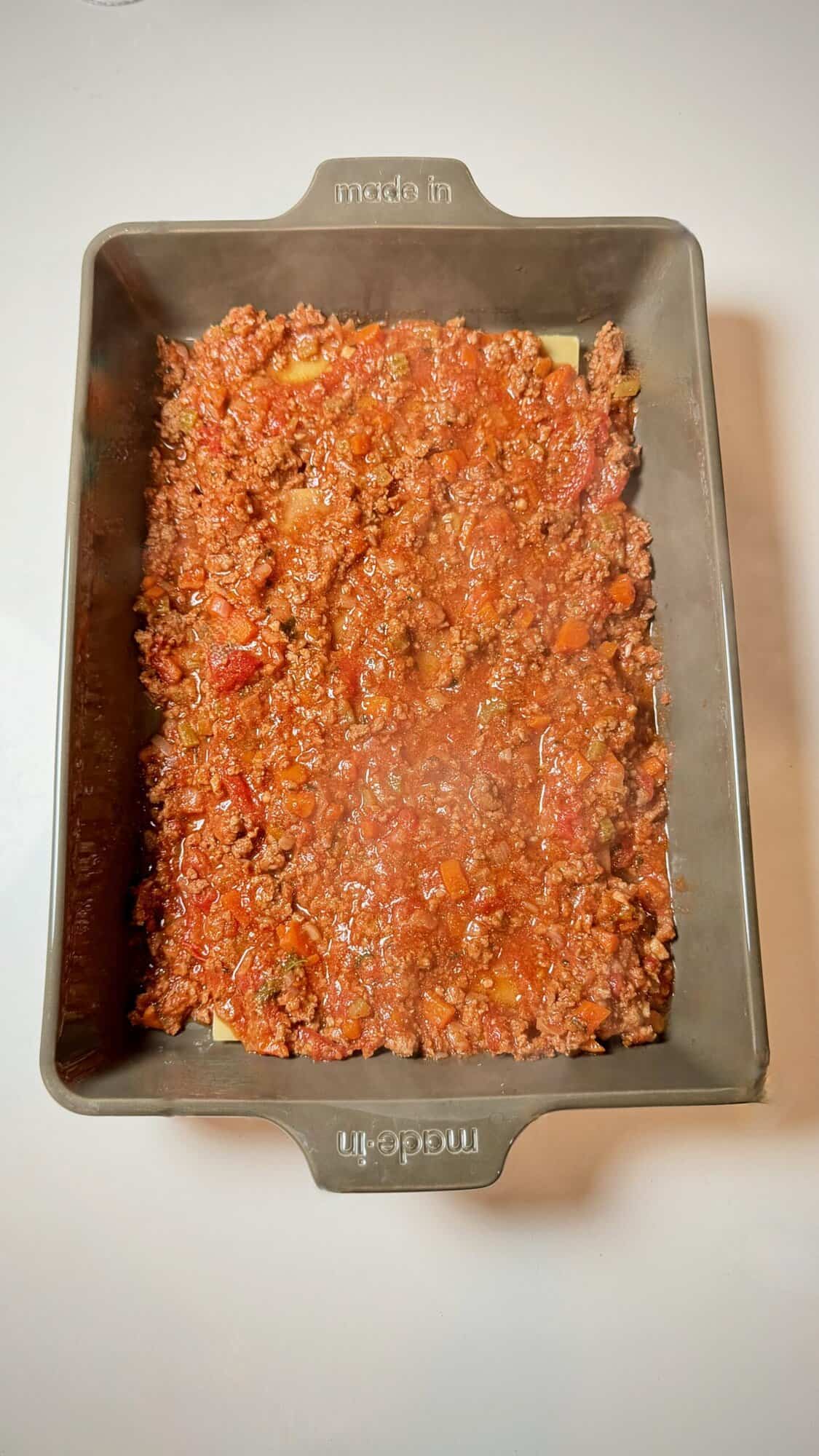 Spreading meat sauce evenly in lasagna baking dish.