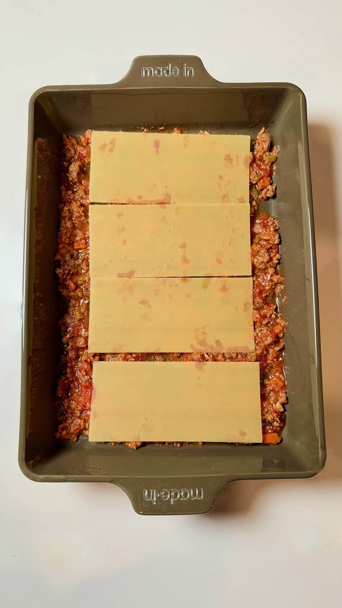 Lasagna noodles on ragu sauce in pan.