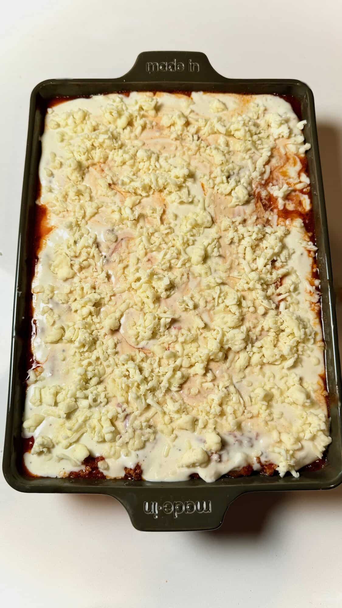 Lasagna with béchamel and mozzarella spread evenly over top layer.