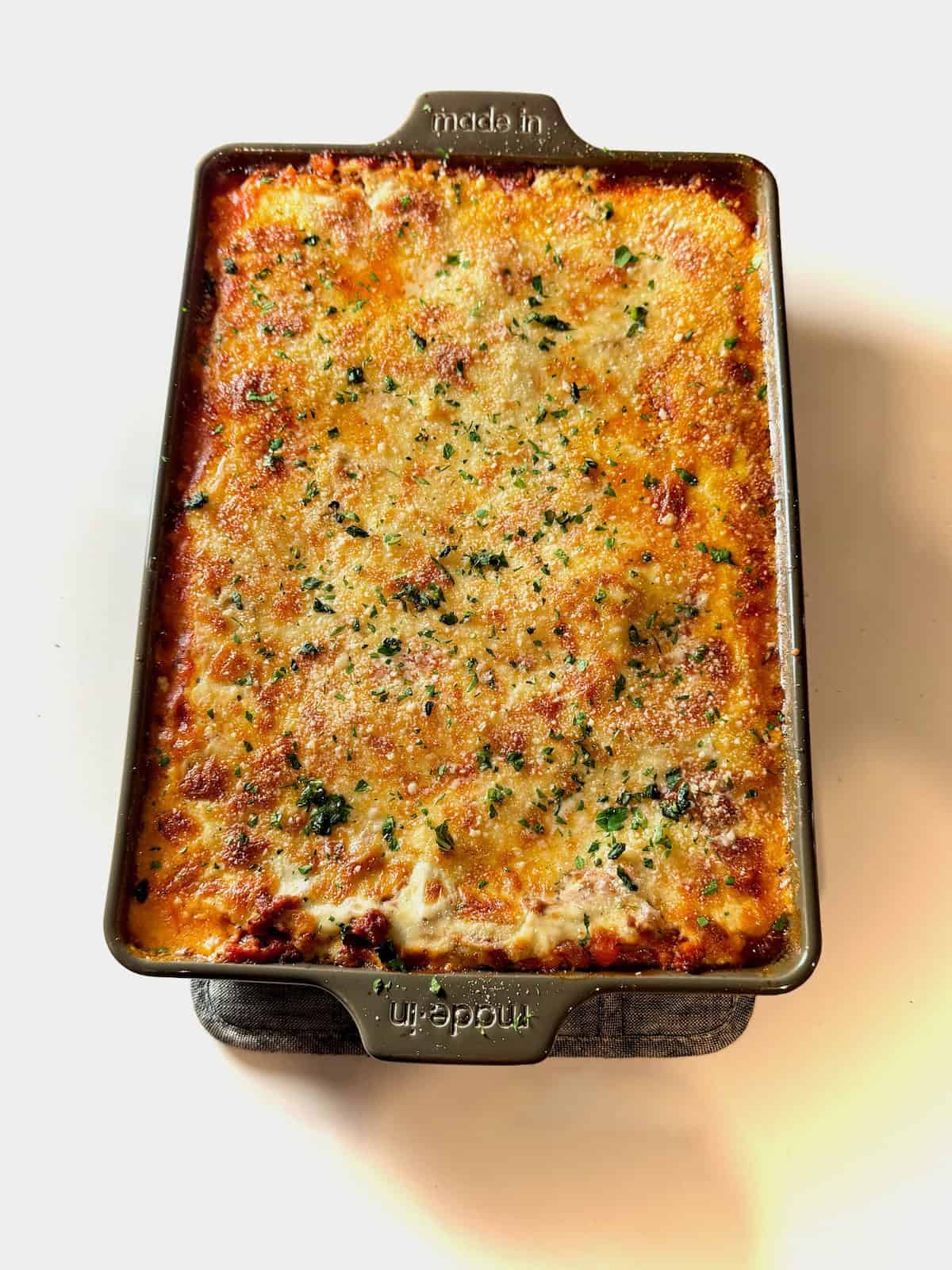 Overhead lasagna with béchamel topped with herbs and cheese.