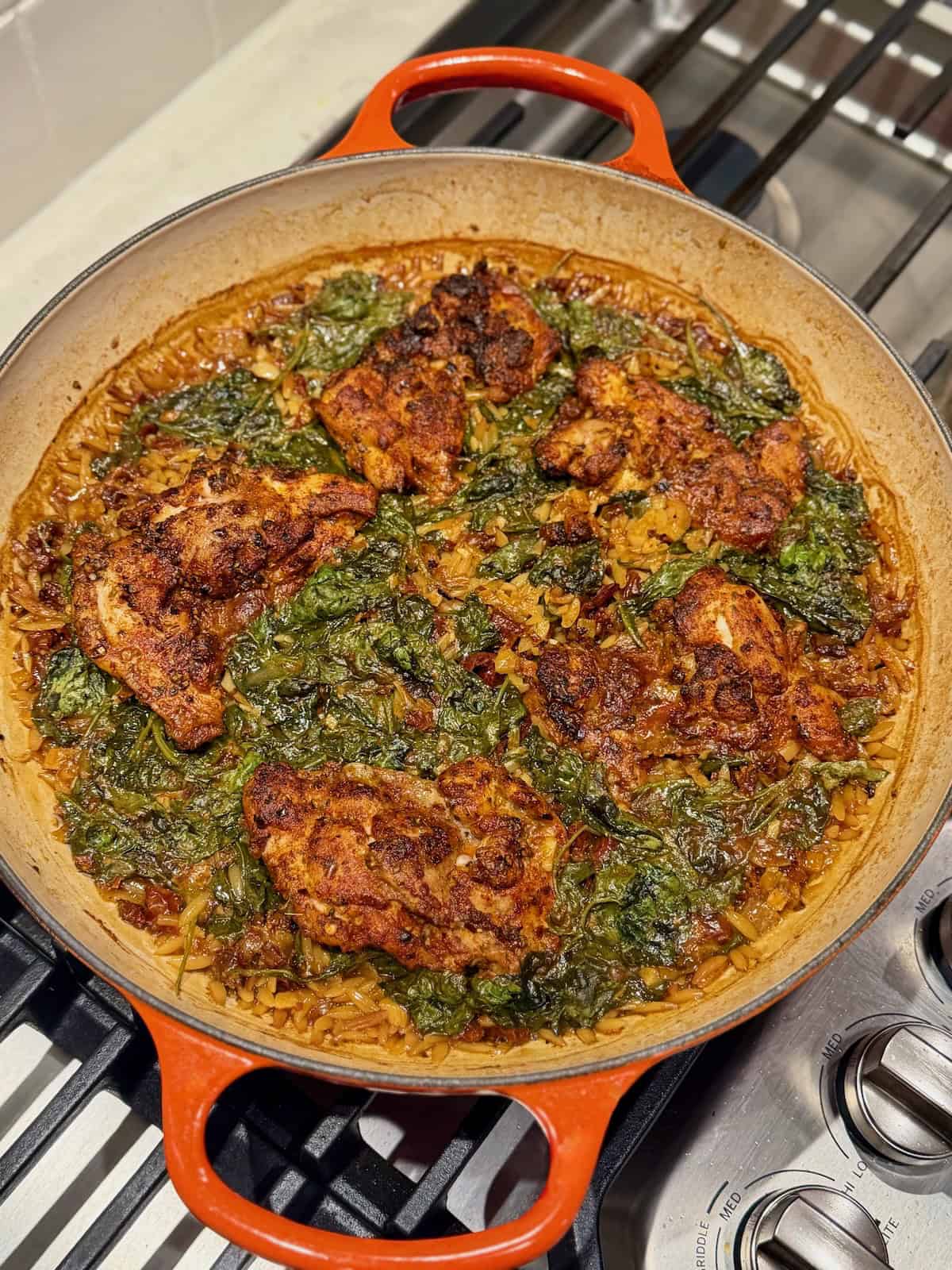 Browned chicken thighs rest over spinach and sun-dried tomato orzo after baking.