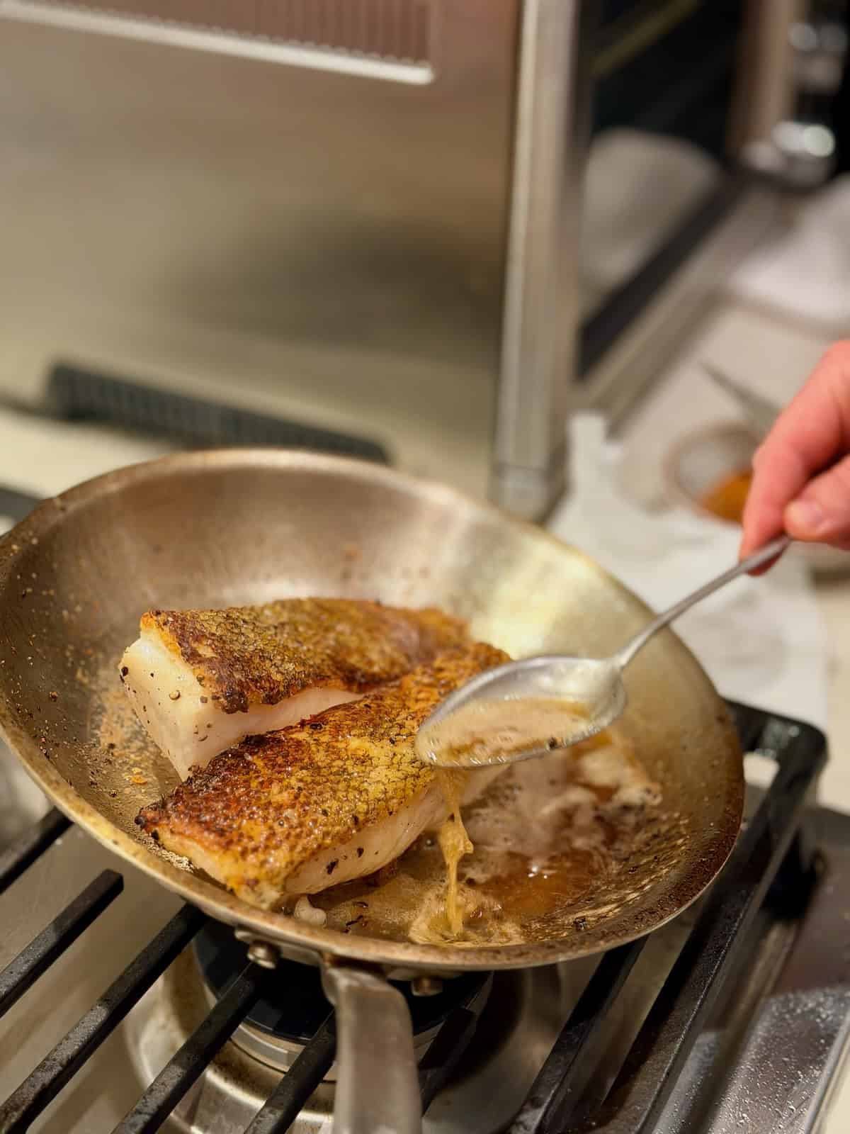 Melted butter is spooned over Chilean sea bass as it finishes cooking.
