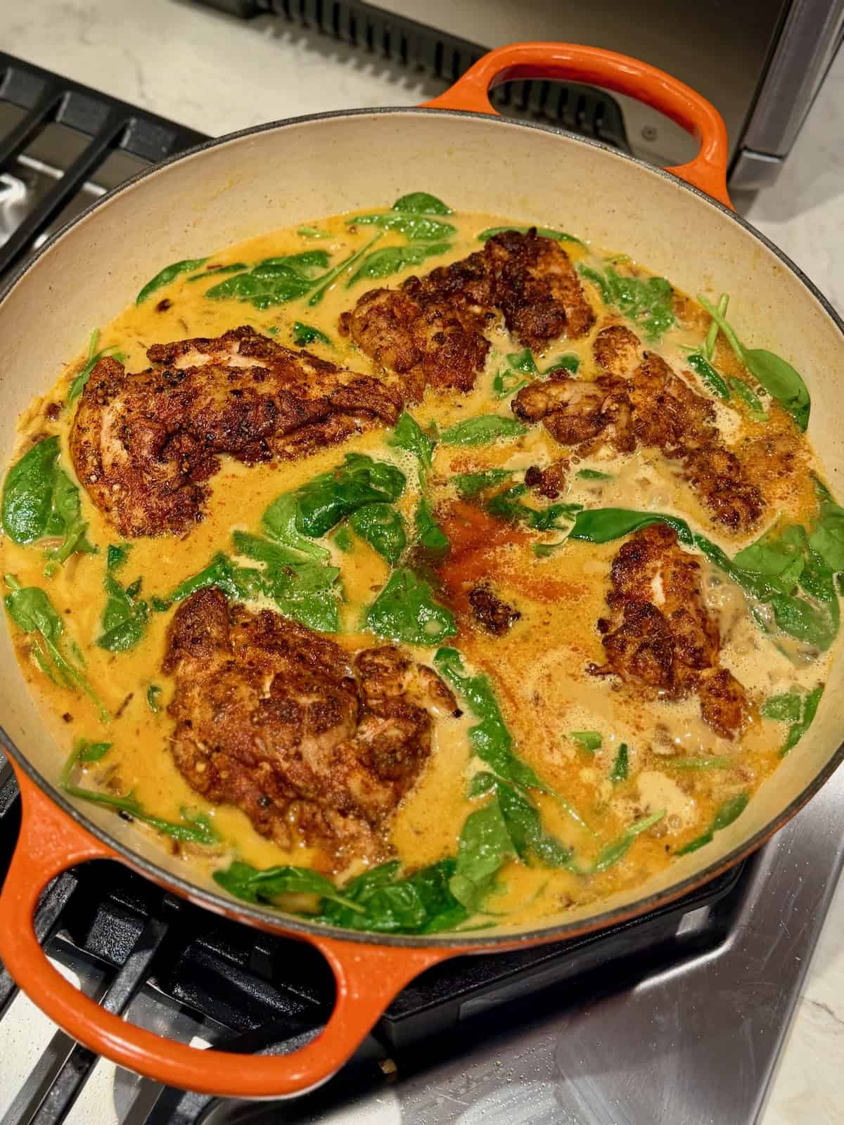 Seared chicken thighs sit in creamy orzo with fresh spinach before the pan goes into the oven.
