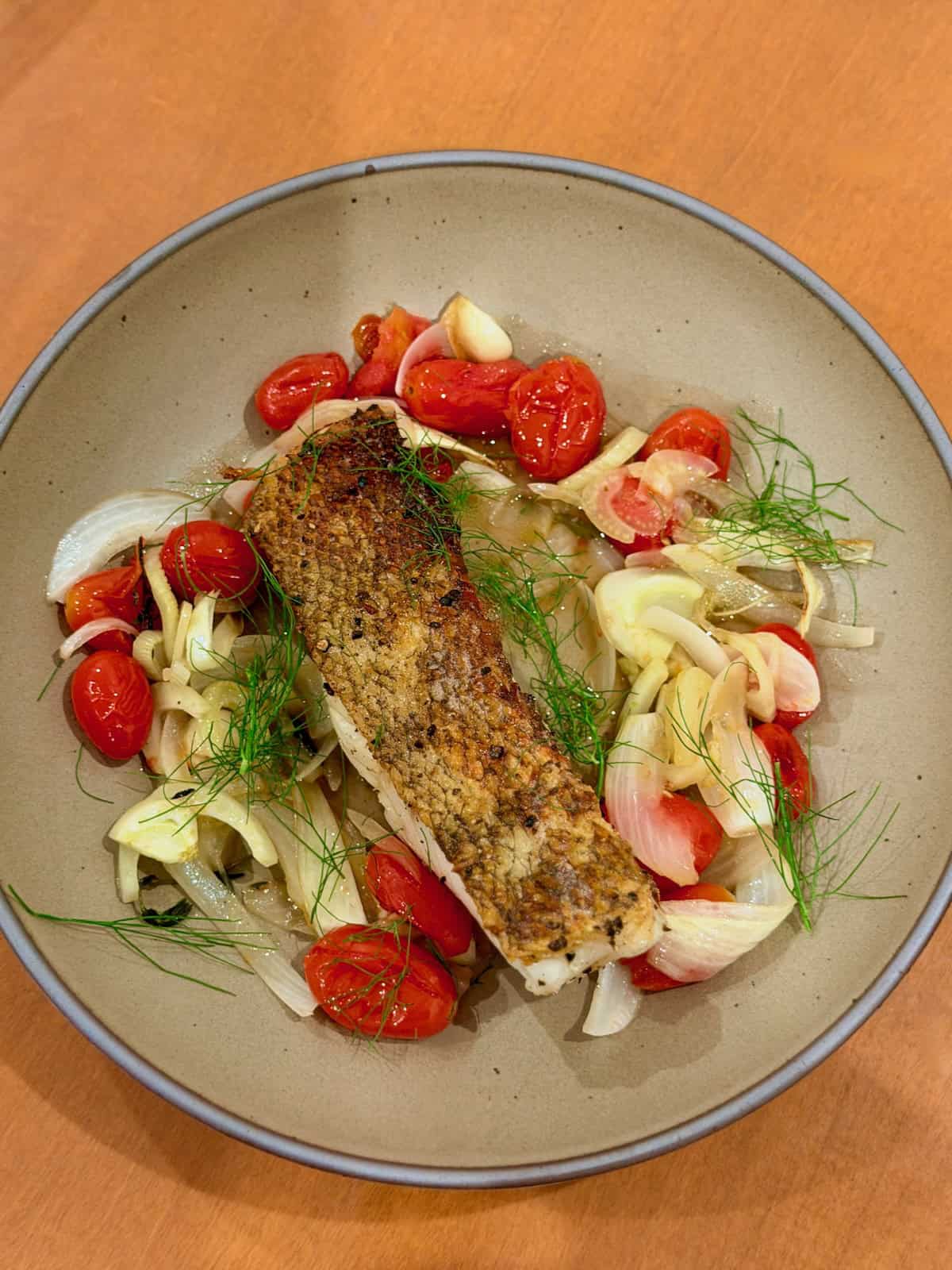 Crispy Chilean sea bass is served over roasted fennel, tomatoes, and onion.