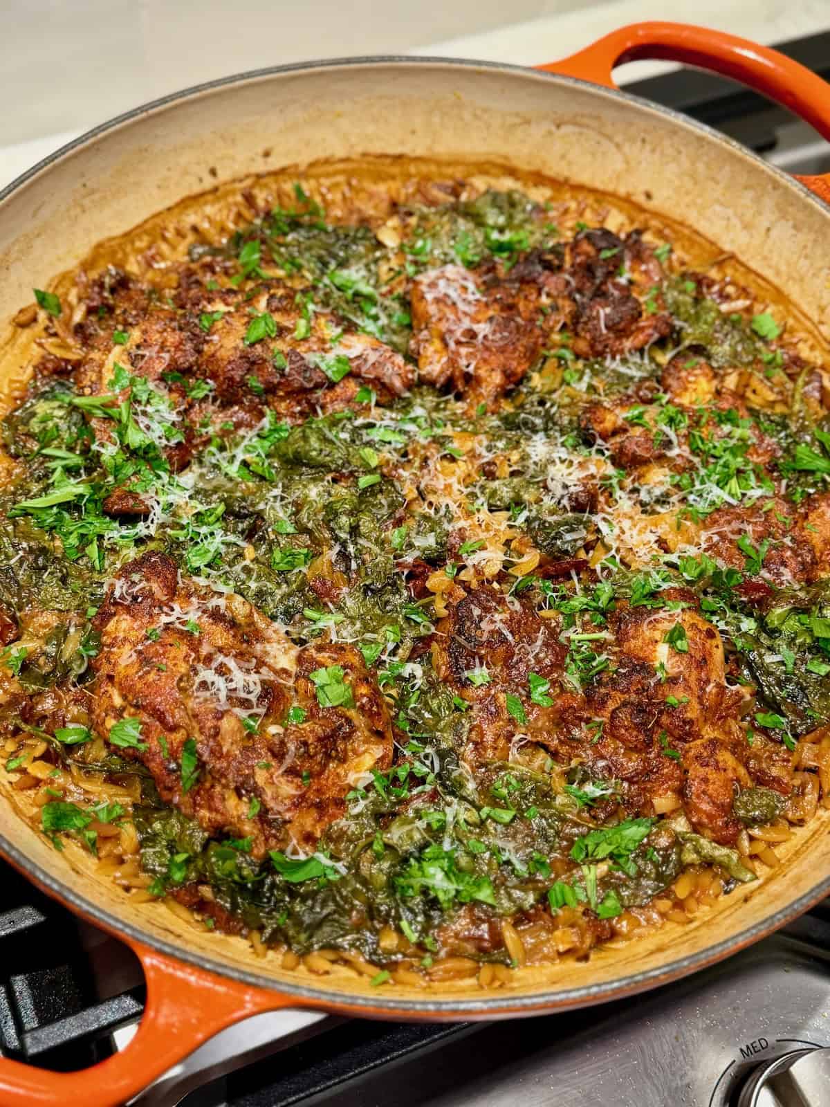 Chicken thighs and spinach orzo are topped with grated Parmesan and chopped parsley in a pan.