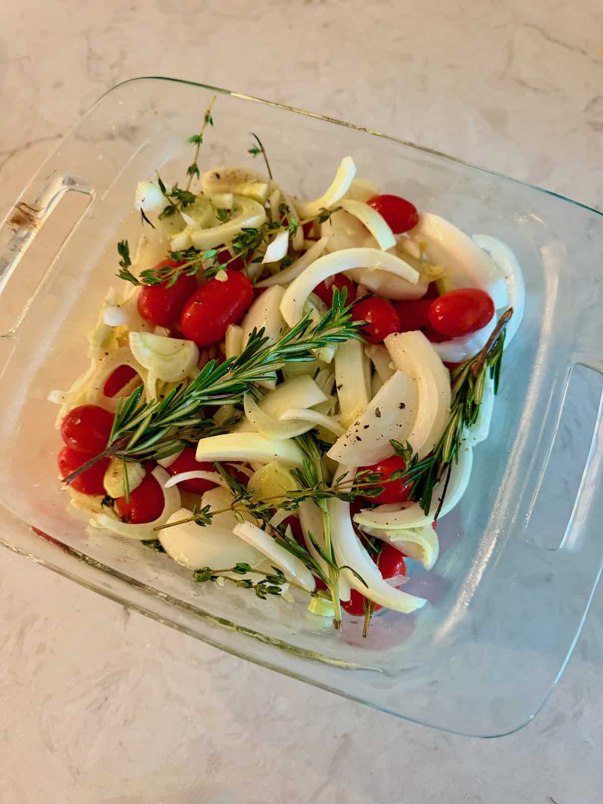 Fennel, cherry tomatoes, onion, garlic, and herbs are ready for roasting in baking dish.