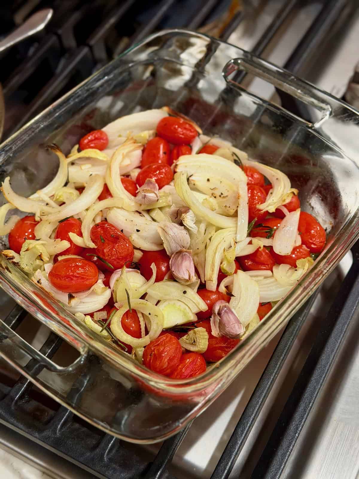 Roasted fennel, cherry tomatoes, onion, and garlic are softened in a baking dish.
