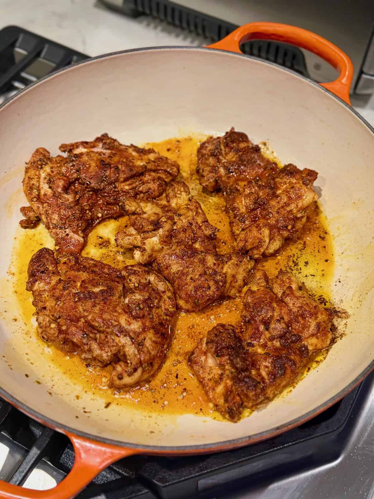 Seasoned boneless chicken thighs develop a dark golden crust as they sear in a pan.