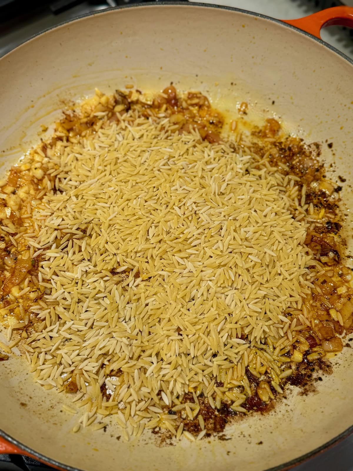 Dry orzo pasta is added to sautéed garlic, shallots, and sun-dried tomatoes in a pan.