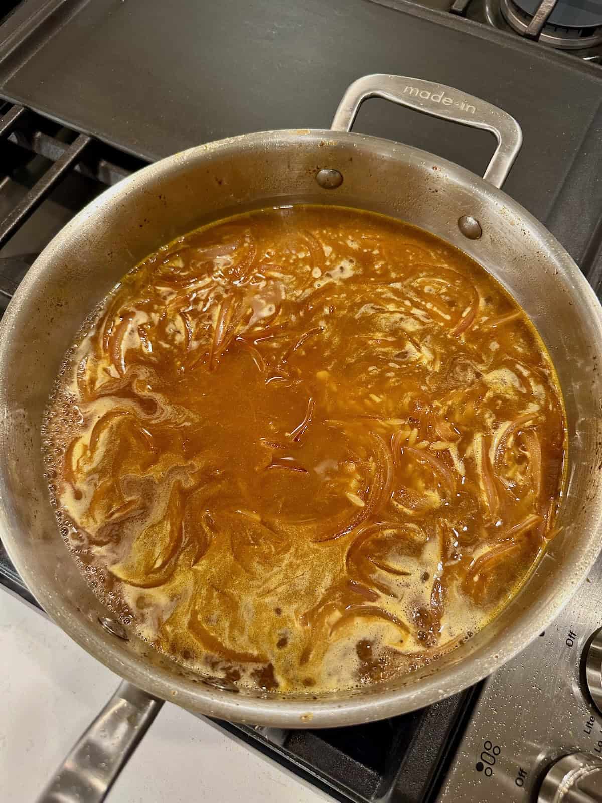 Orzo simmering in broth in a skillet for chicken shawarma orzo.