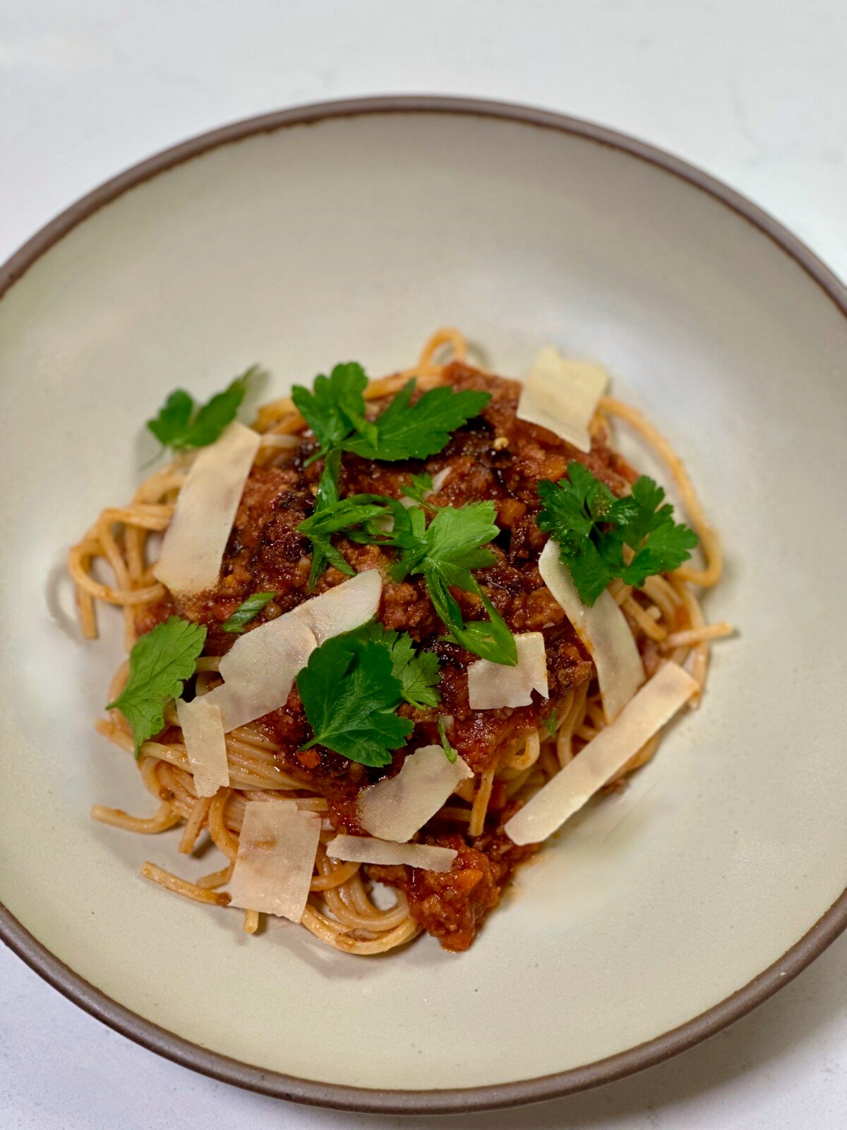 A bowl of pasta with red sauce, strips of parmesan cheese, and pieces of parsley
