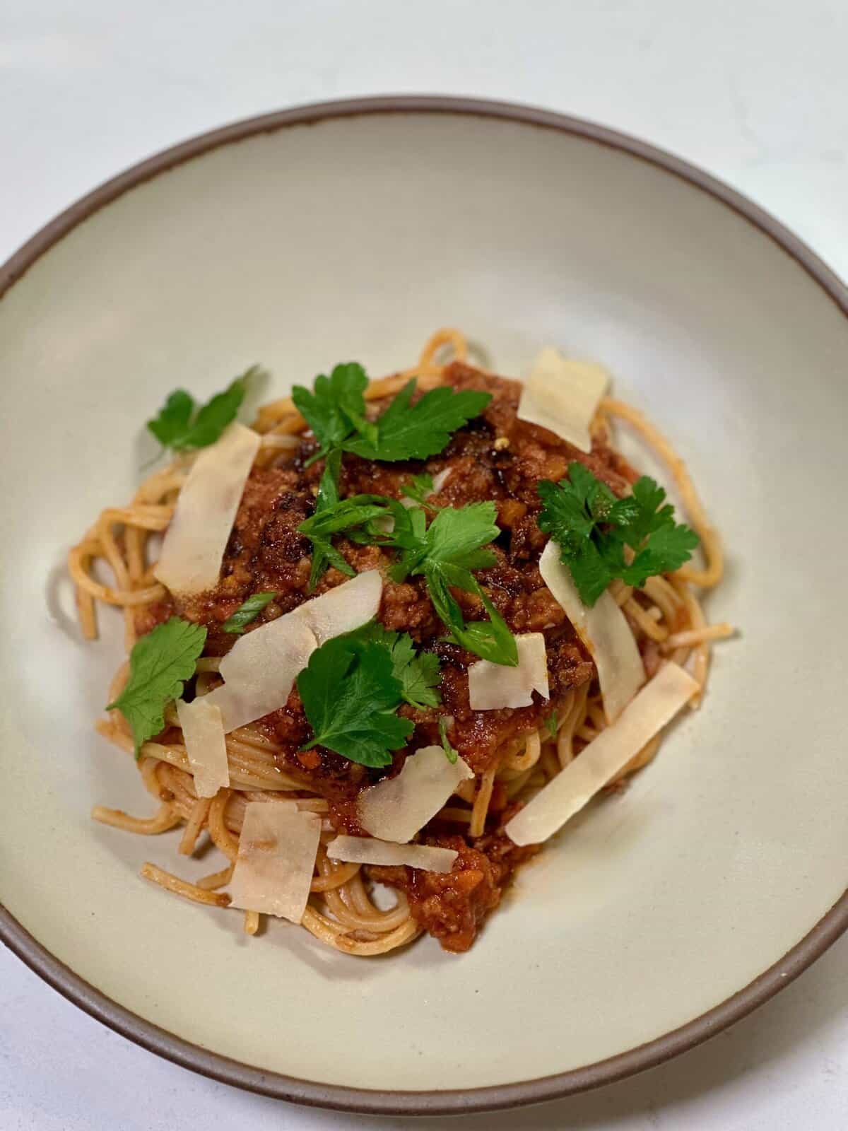 A bowl of pasta with red sauce, strips of parmesan cheese, and pieces of parsley.