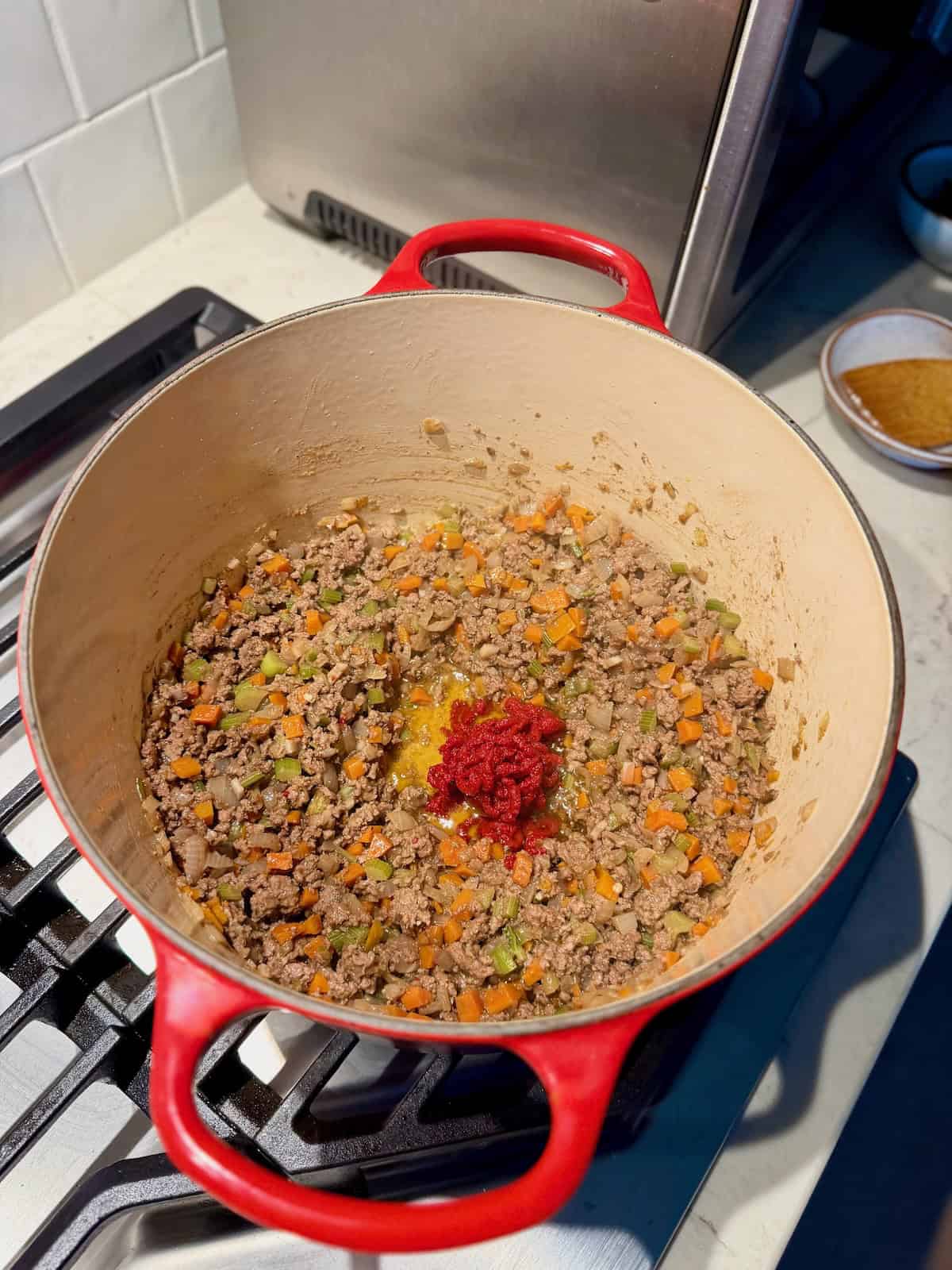 Browned ground beef and vegetables cook with tomato paste in a Dutch oven.