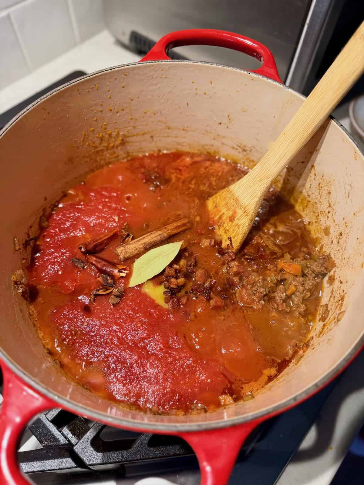 Tomatoes, cinnamon, bay leaf, and toasted spices are added to the browned beef.