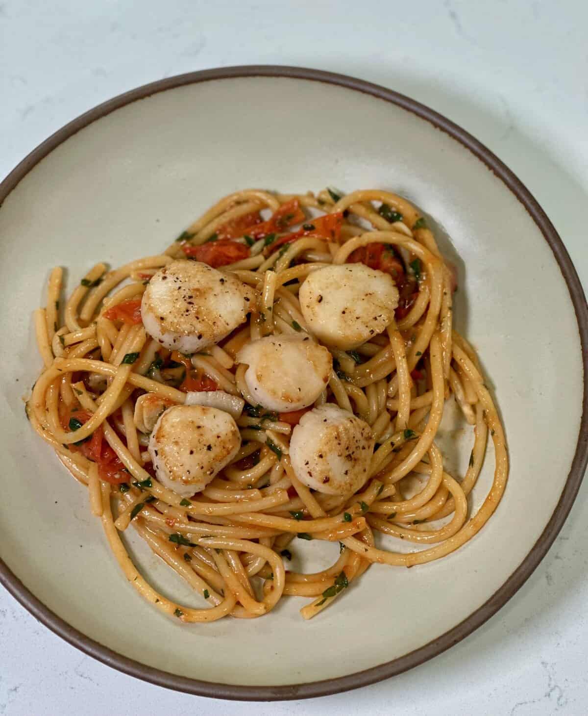 a white bowl with bucatini pasta, burst tomatoes, and seared scallops