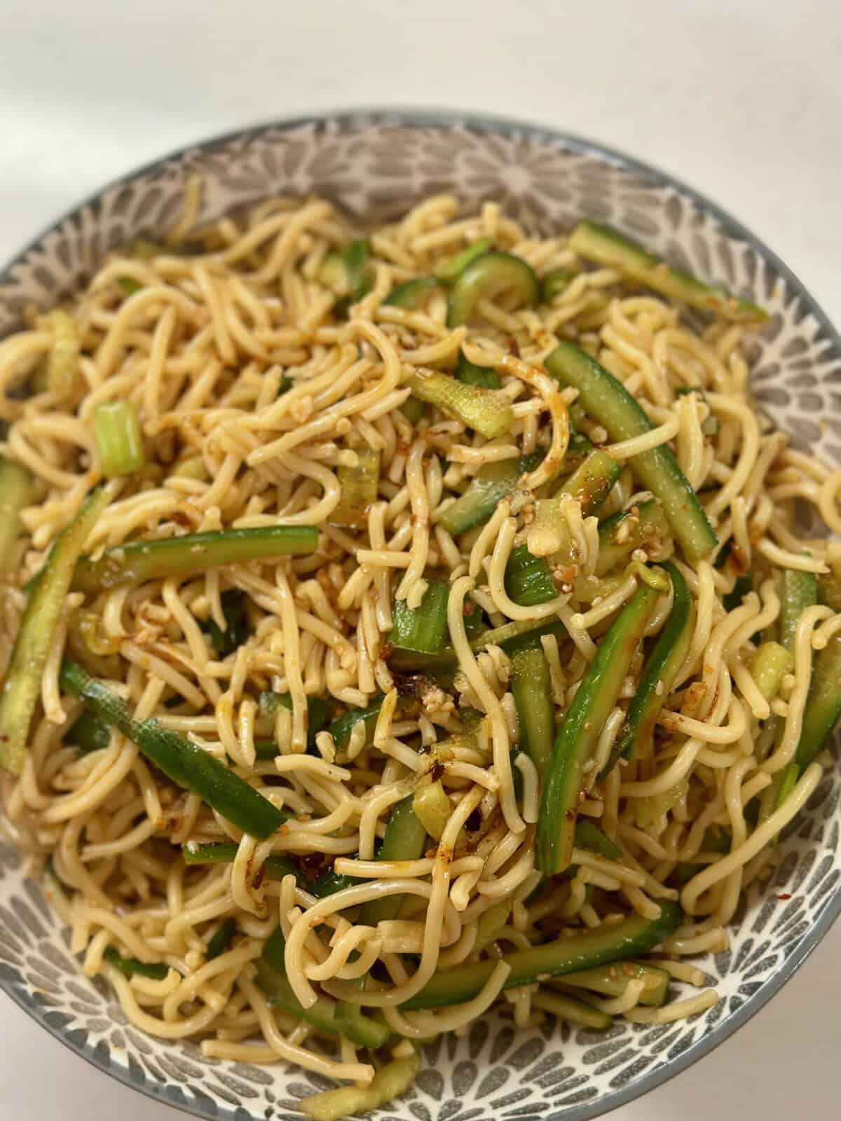 A bowl with noodles, cucumbers, with a spicy sauce