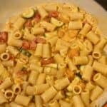 A pan with zucchini, tomatoes, corn, and creamy pasta