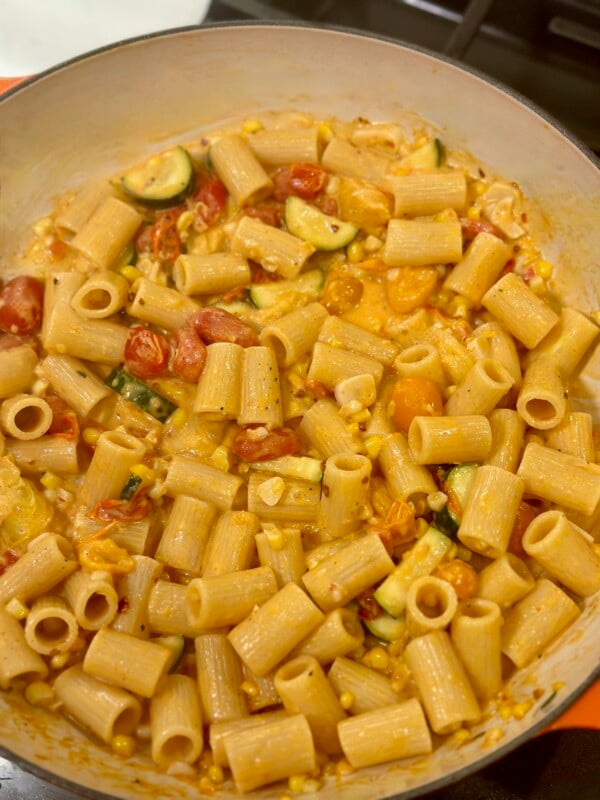 A pan with zucchini, tomatoes, corn, and creamy pasta