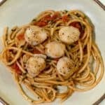 Bursted tomato pasta with seared scallops served on white plate.