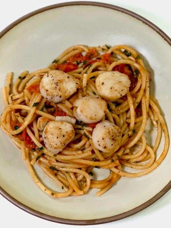 Bursted tomato pasta with seared scallops served on white plate.
