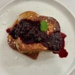 A white plate with Brioche French Toast, blueberry compote, and mint leaves