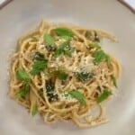 A white bowl with spaghetti tossed in a zucchini sauce topped with cheese and basil