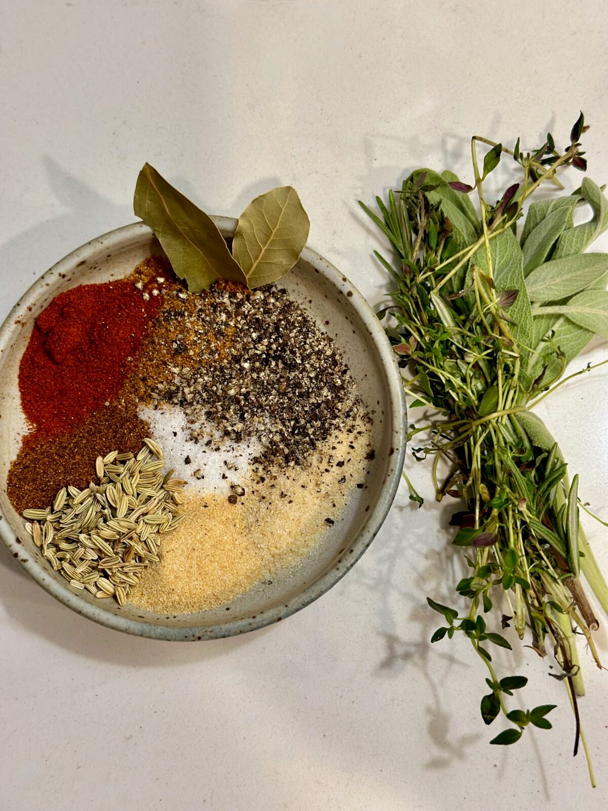 A small bowl with dry spices and a bundle of fresh herbs tied together