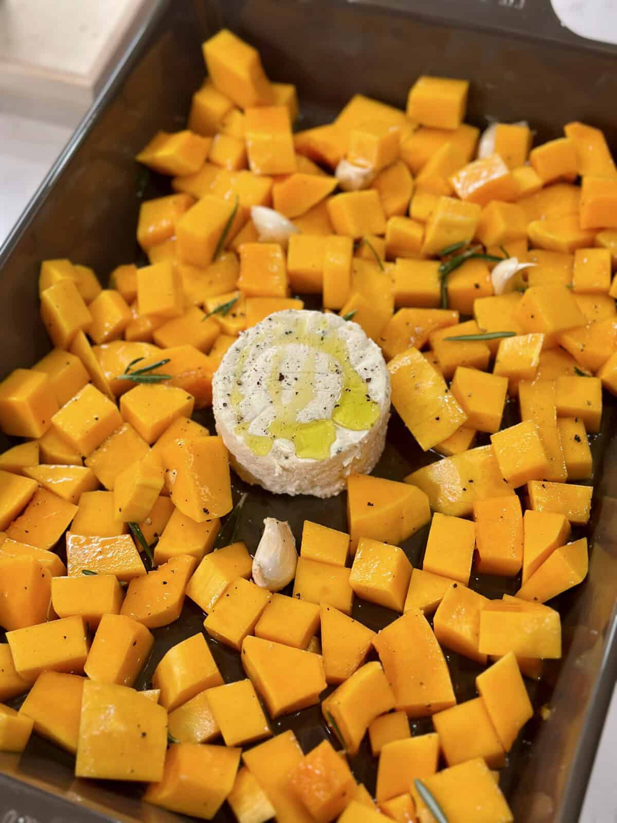 A baking dish with cubed butternut squash and a block of boursin in the middle