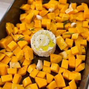 A baking dish with cubed butternut squash and a block of boursin in the middle