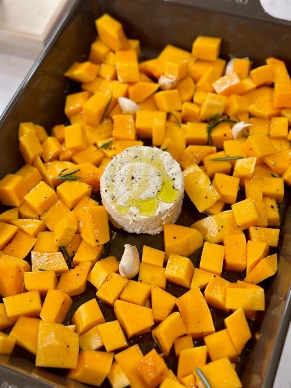 A baking dish with cubed butternut squash and a block of boursin in the middle