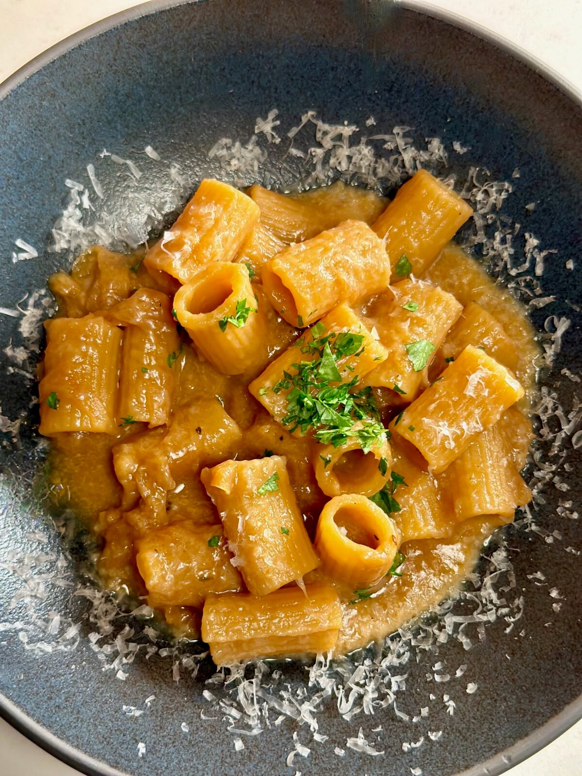 Blue bowl with french onion pasta topped with parmesan cheese and parsley