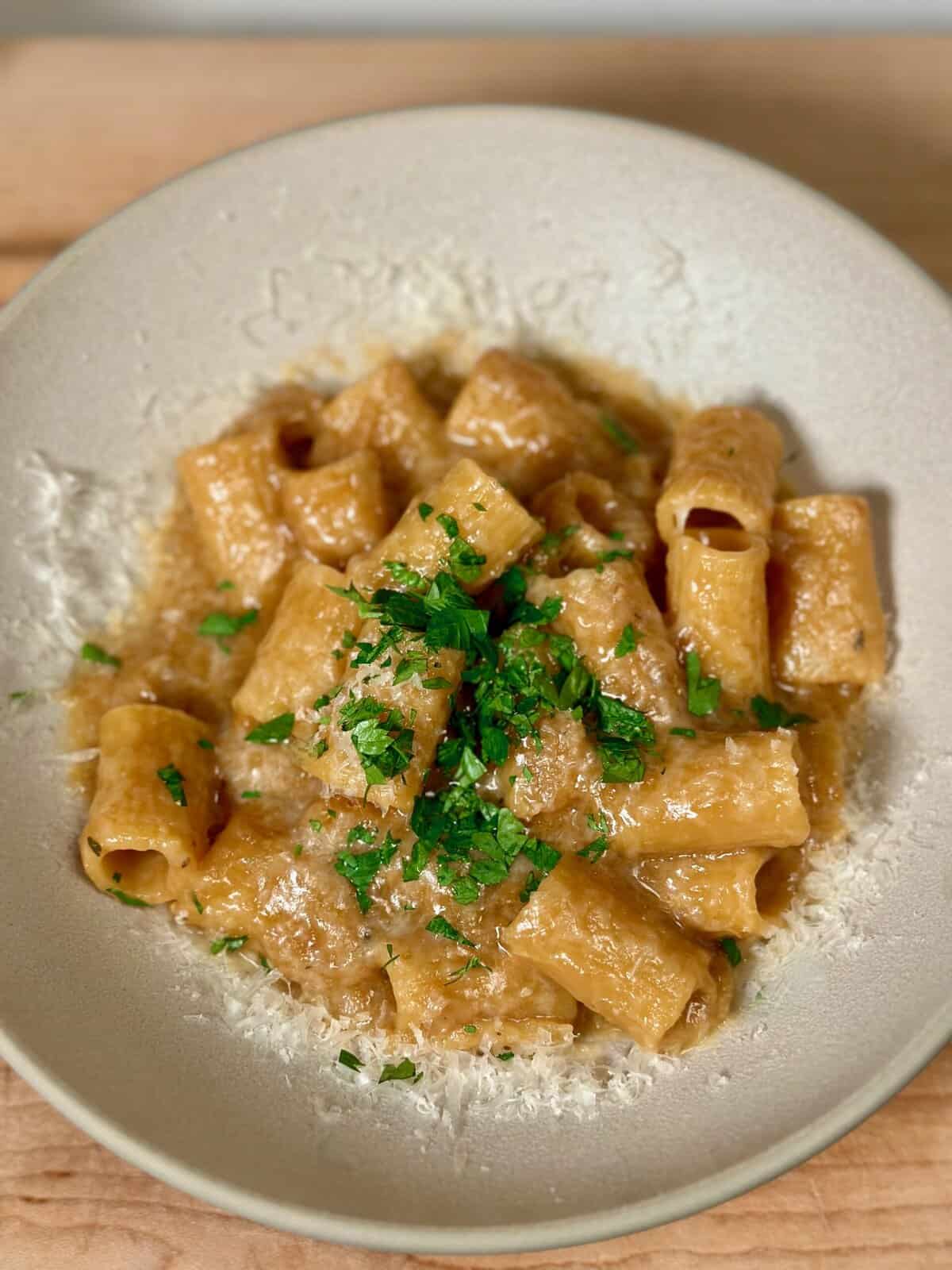 A white bowl with french onion pasta sprinkled with parmesan and parsley.