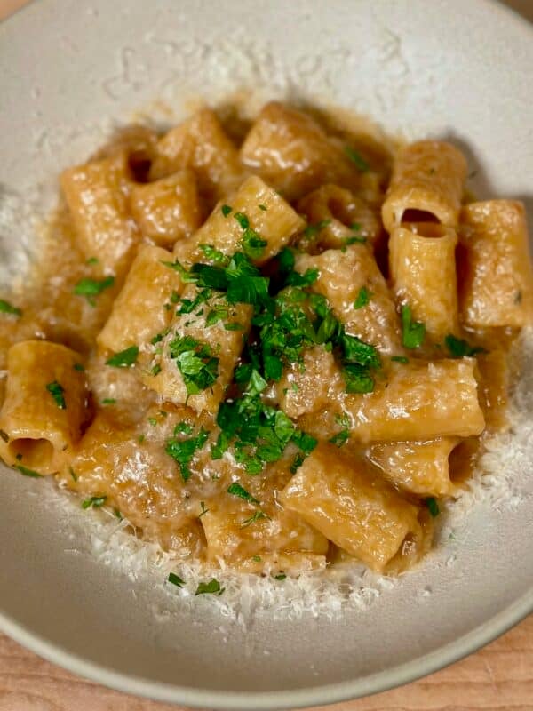 One pot french onion pasta in a bowl sprinkled with parsley and freshly grated parmesan cheese.