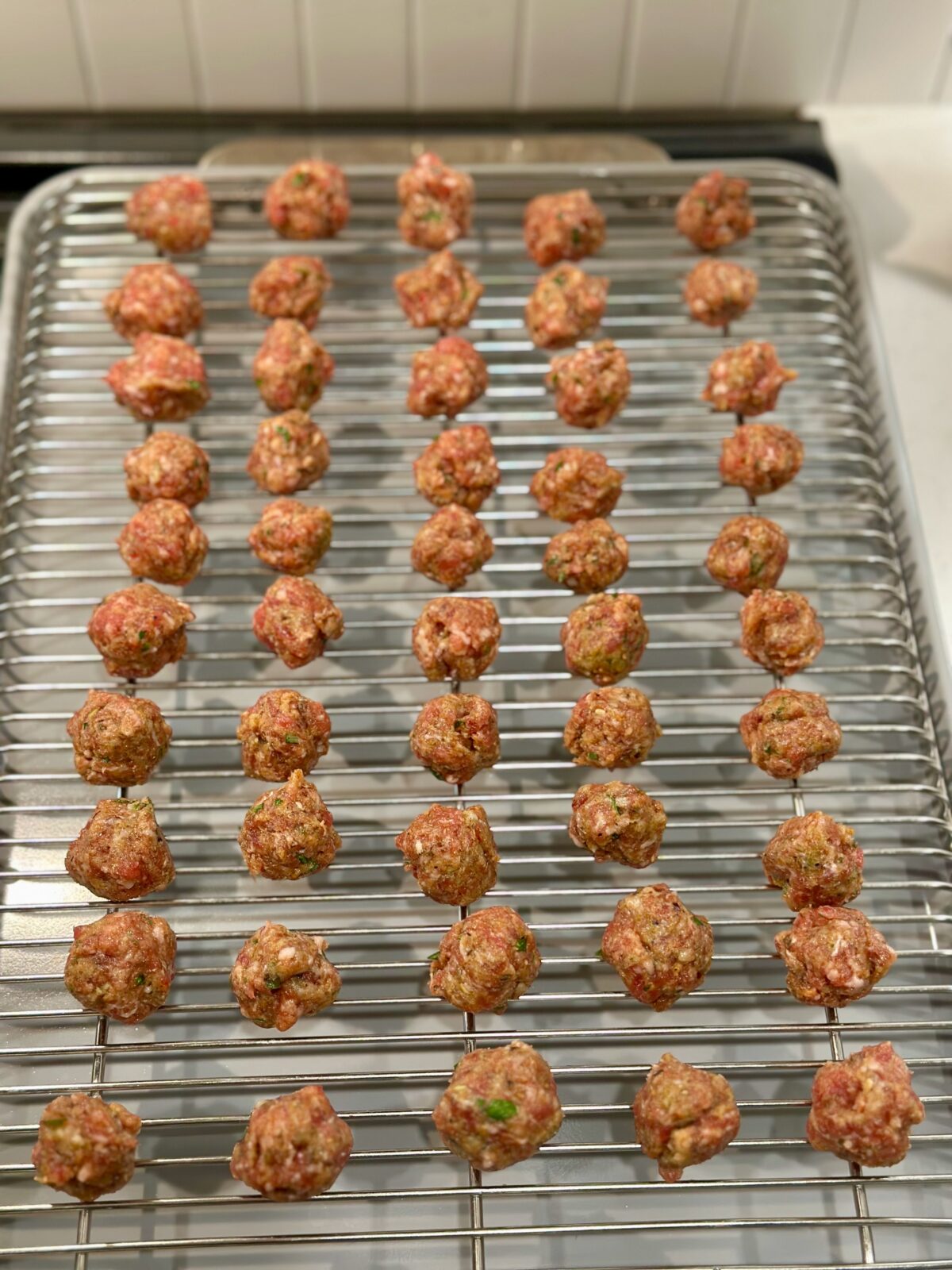 Baking sheet with wire rack and raw Italian sausage meatballs for mini meatball soup.
