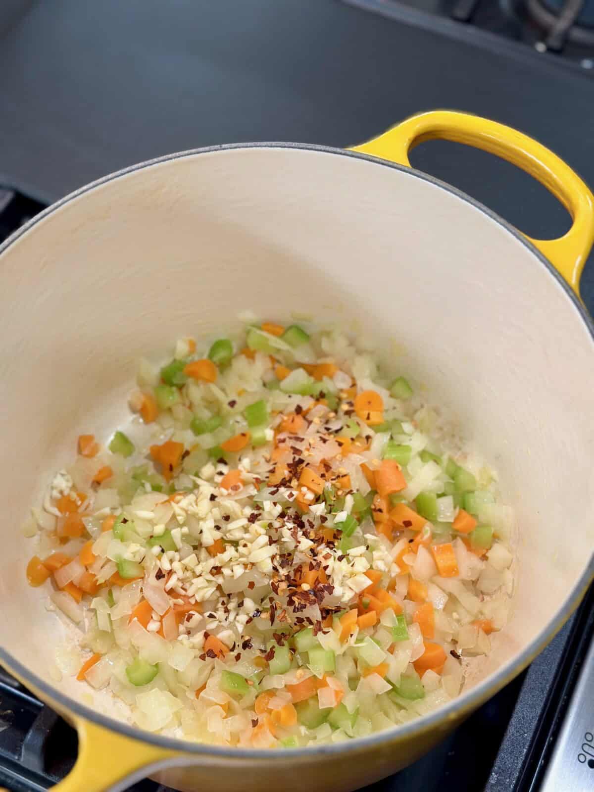 Yellow Dutch Oven with onions, celery, carrots, garlic, and red pepper flakes