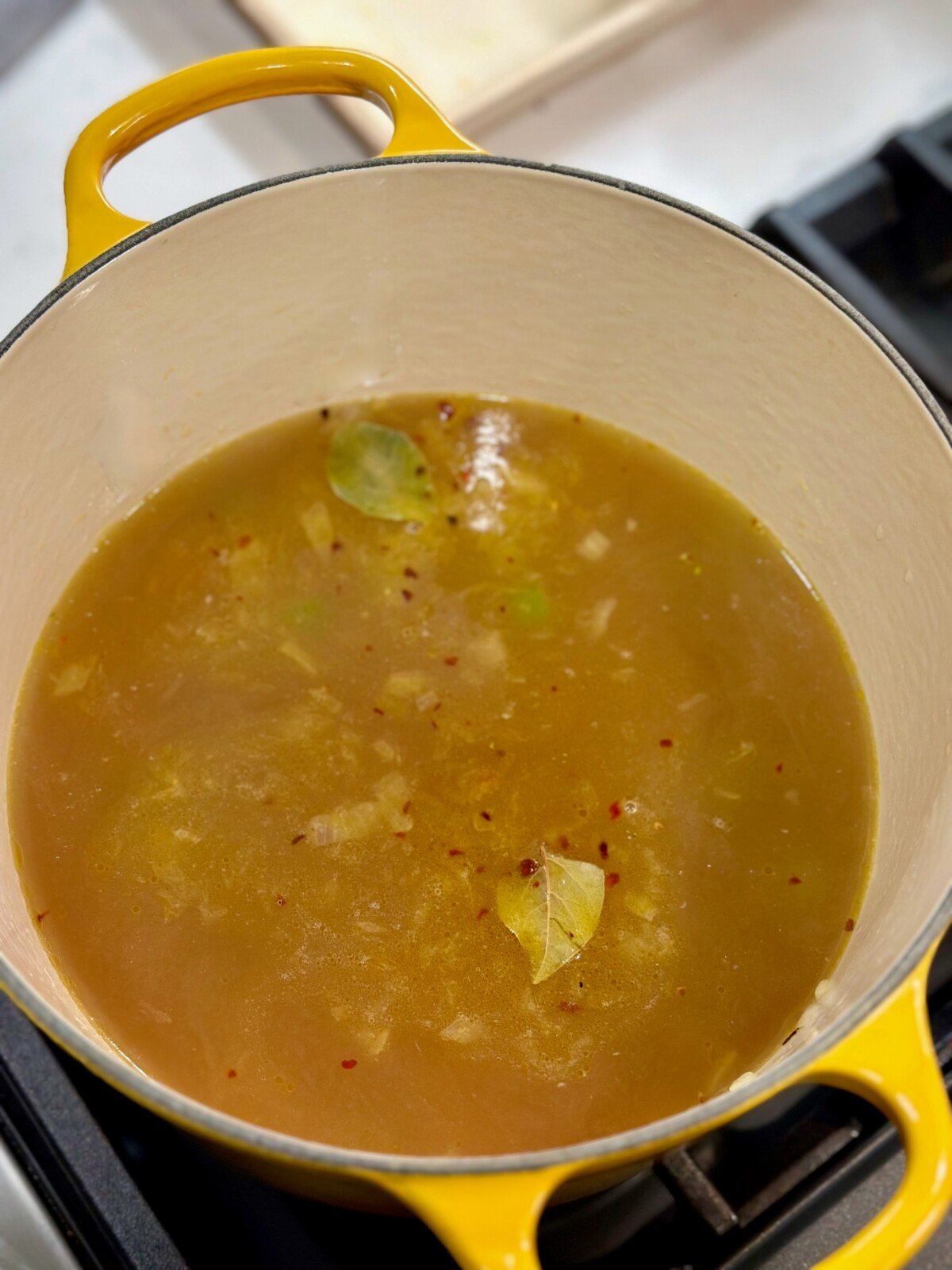 Yellow Dutch Oven with chicken broth and bay leaf