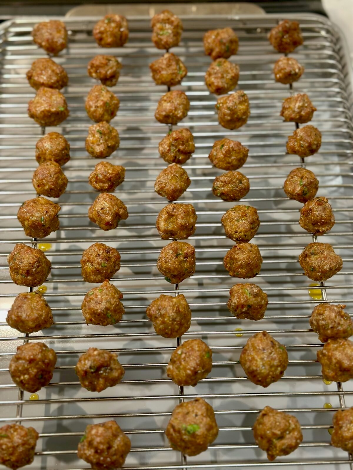 Baking sheet with wire rack and cooked Italian sausage meatballs for mini meatball soup.