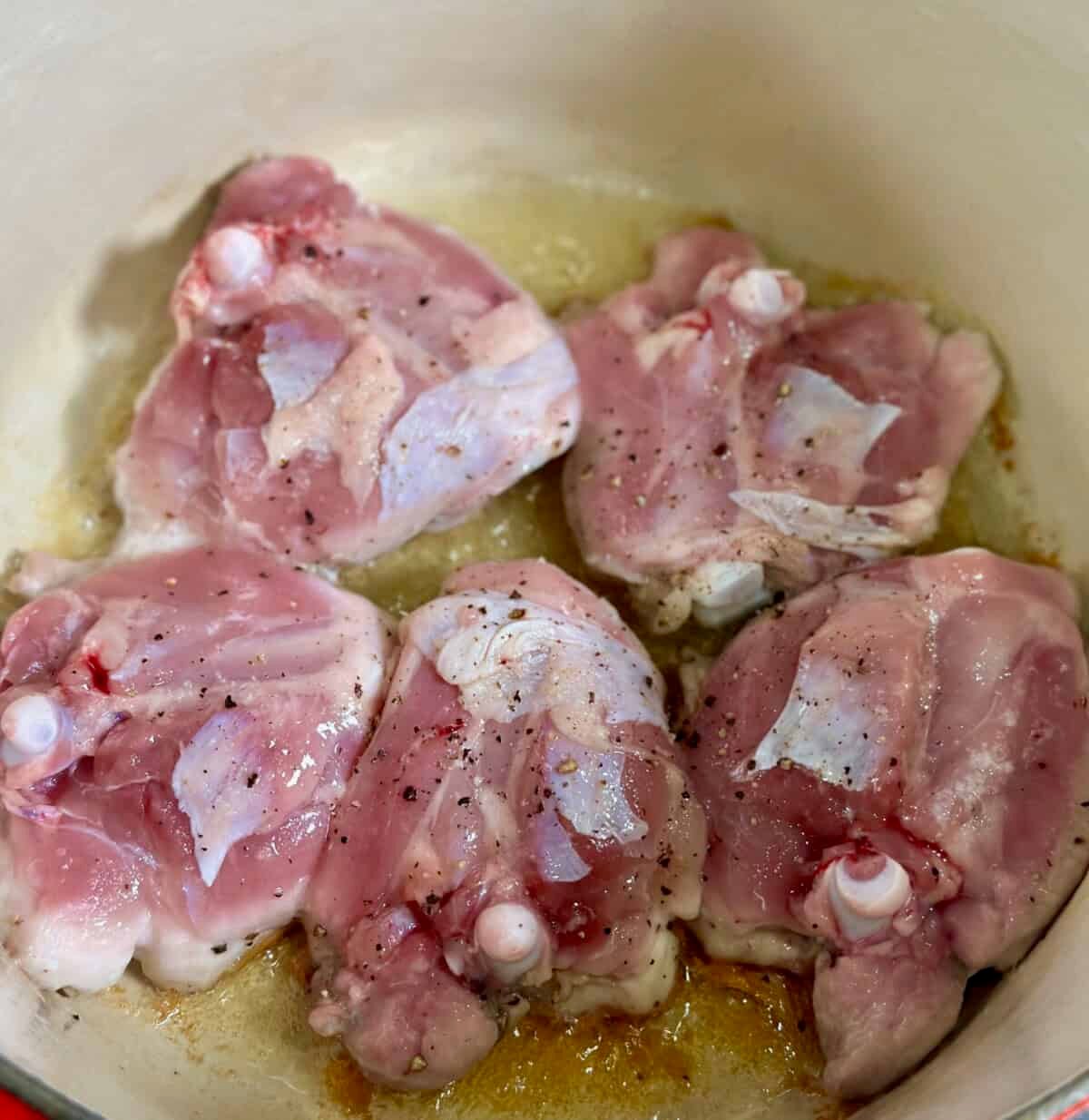 Dutch oven with 5 raw bone-in, skin-on chicken thighs seasoned with salt and pepper