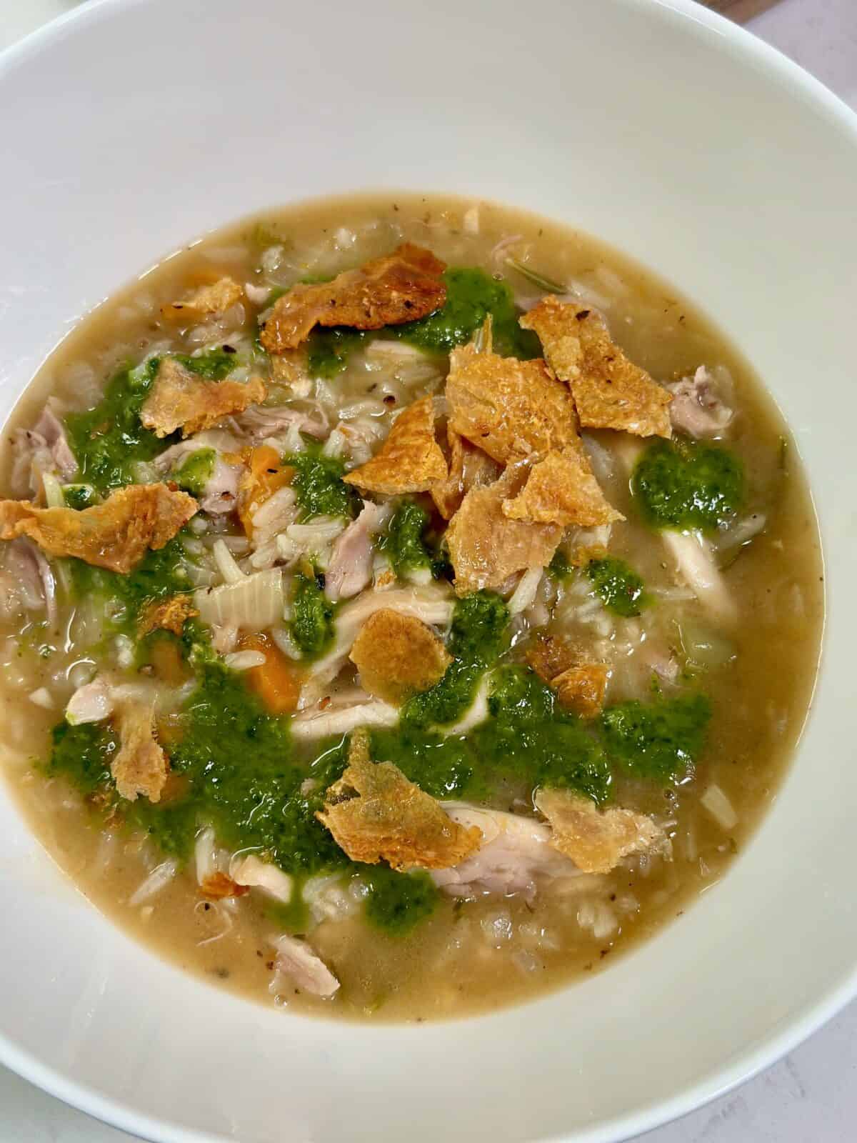 White bowl with herby chicken and rice with herb sauce and crumbled crispy chicken skins