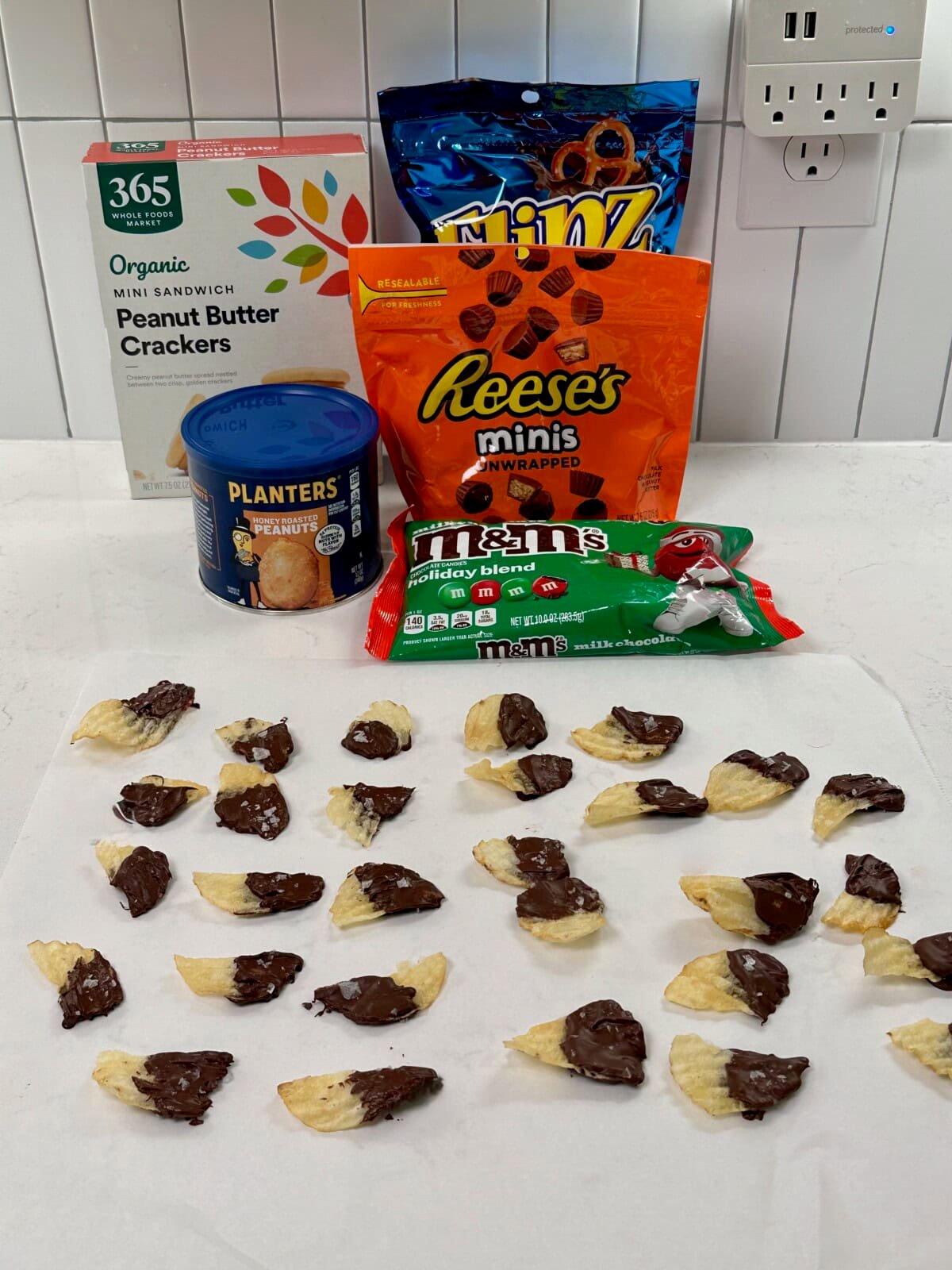 Box of mini peanut butter sandwich crackers, container of honey roasted peanuts, bag of chocolate covered pretzels, bag of mini reese's, bag of holiday m&m's, and chocolate covered potato chips