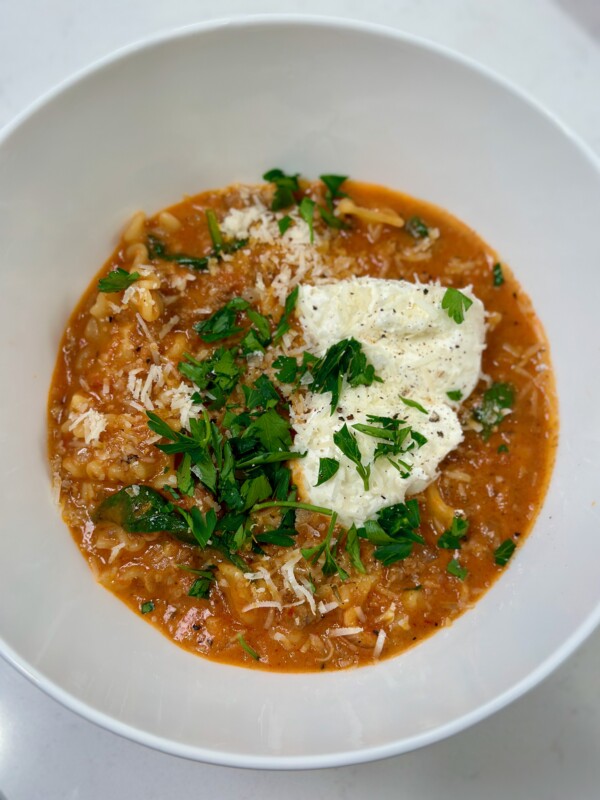 White bowl with lasagna soup, ricotta, and basil