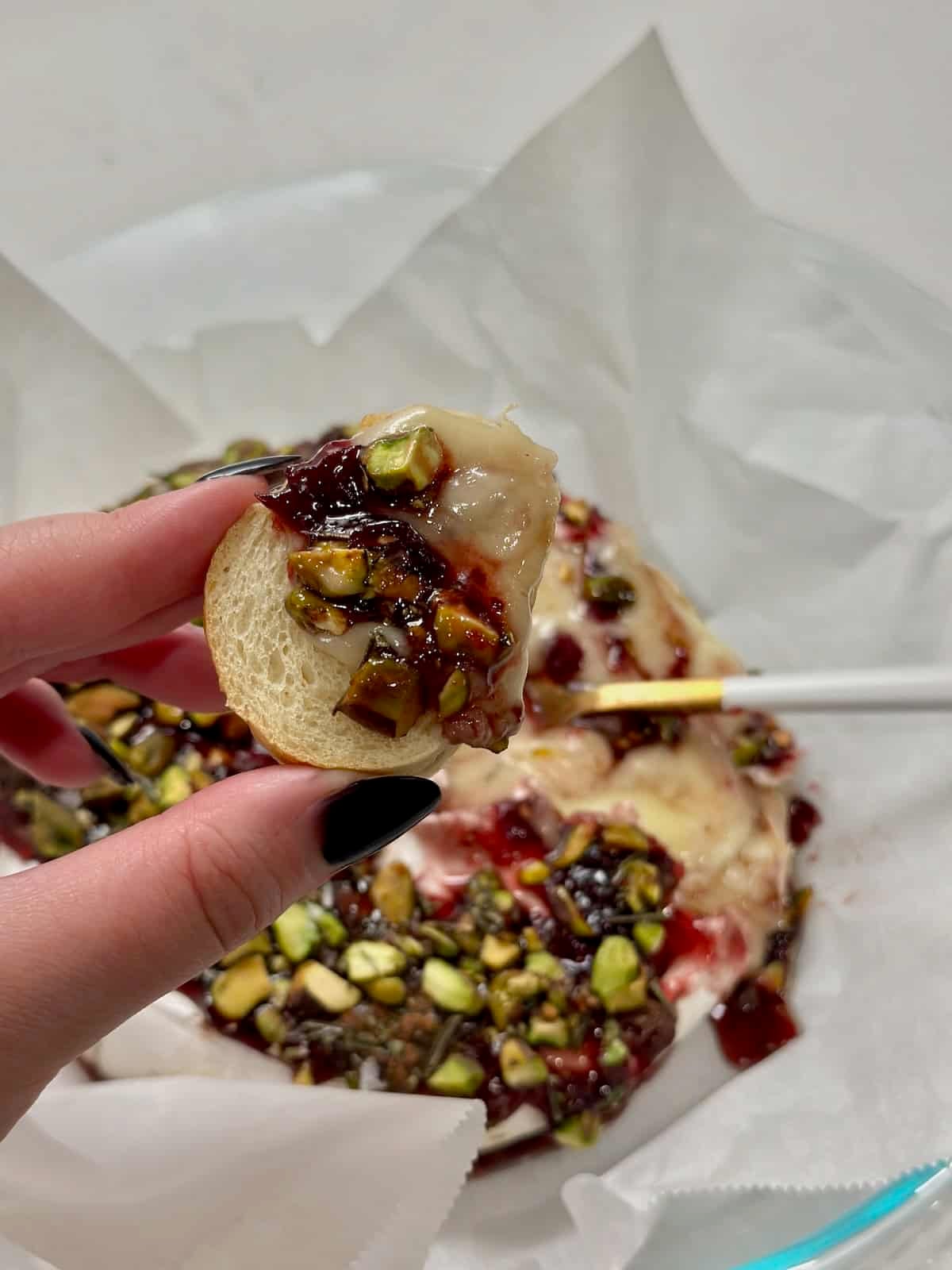 Warm baked brie with cherry preserves and pistachios spread onto a baguette slice.