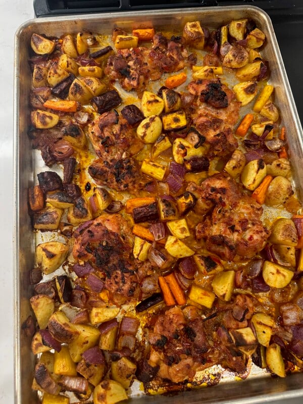 Cooked harissa chicken thighs and vegetables on sheet pan