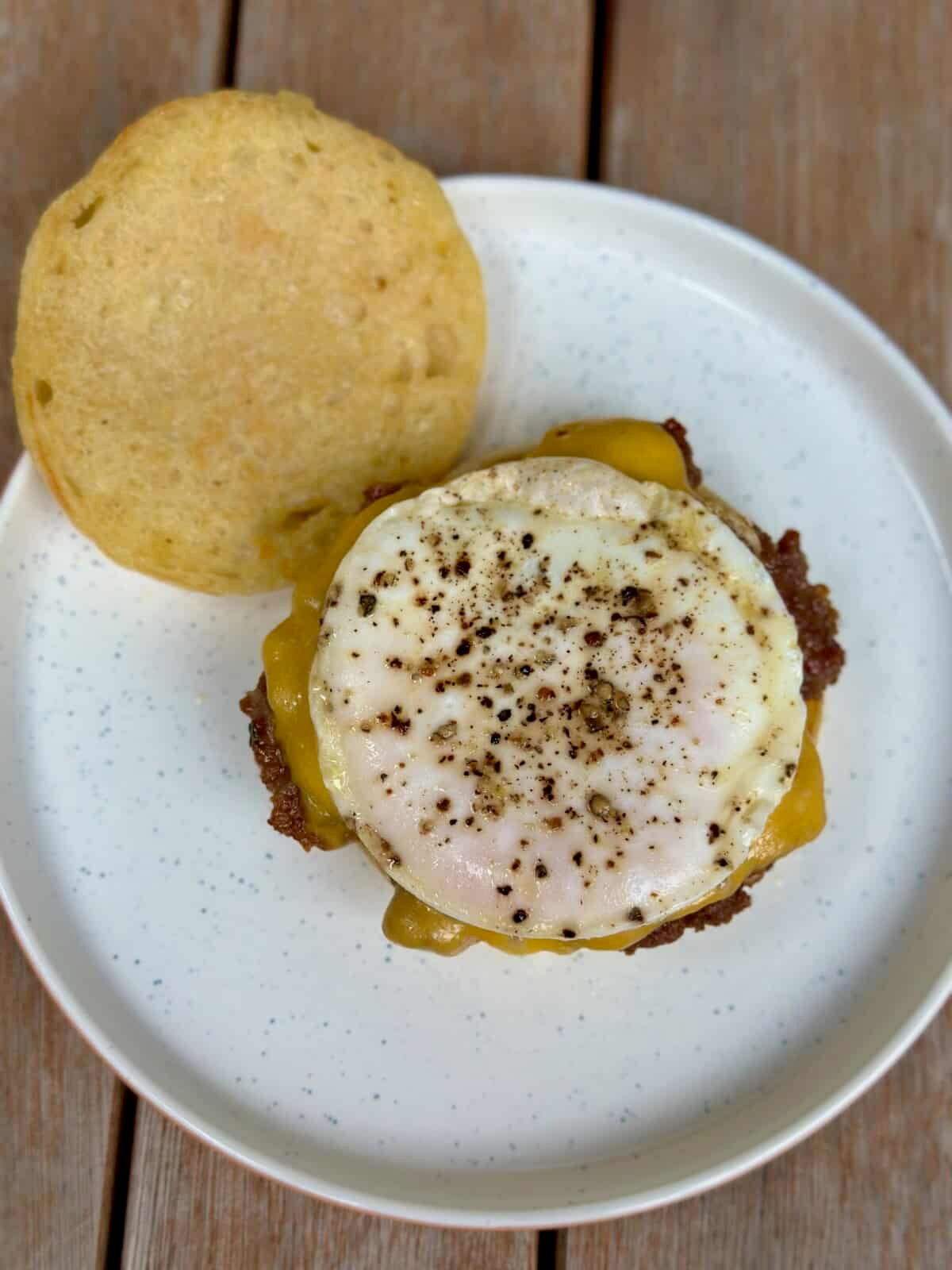 A plate with a sausage patty, seasoned egg, and english muffin