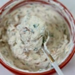 Creamy caramelized shallot dip on a spoon lifted from bowl.