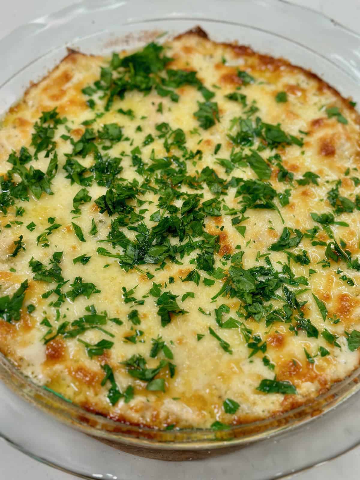 Baked chicken alfredo dip garnished with parsley.