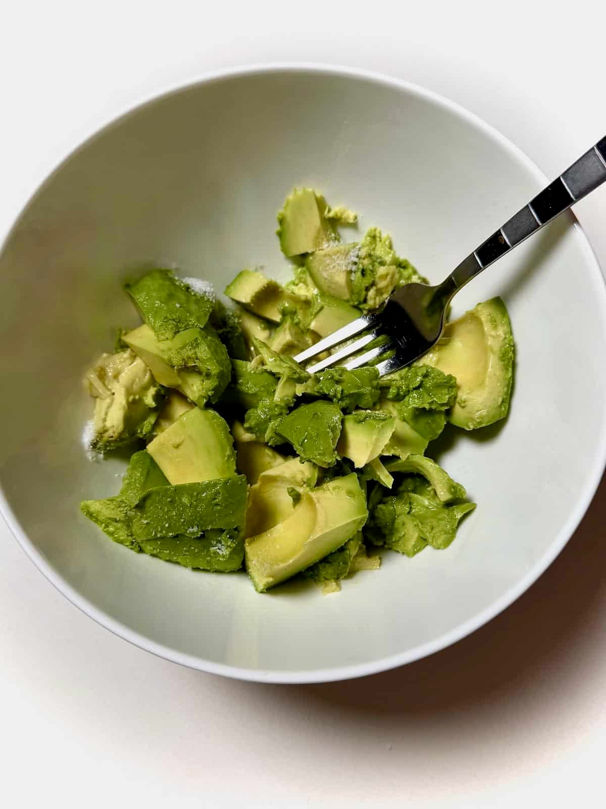 Avocado and salt in bowl smashed with a fork.